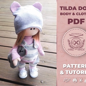 May include: A gray and pink Tilda doll with a gray hat and a striped dress. The doll is holding a gray stuffed animal. The image includes the text "Tilda Doll Body & Clothes PDF Pattern & Tutorial PDF"