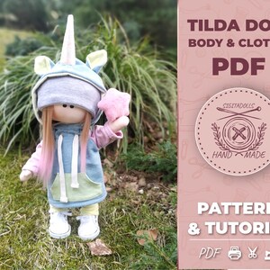 May include: A PDF pattern and tutorial for making a Tilda doll with a unicorn-themed outfit. The doll is wearing a blue hooded sweatshirt with a yellow pocket, pink sleeves, and a unicorn horn and ears. The doll is holding a pink star. The text "TILDA DOLL BODY & CLOTHES PDF" and "PATTERN & TUTORIAL PDF" is visible in the image.