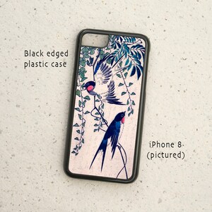 Könnte beinhalten: Schwarze Handyhülle mit weißem Hintergrund und einem Design aus zwei blauen und weißen Vögeln, die auf einem Zweig mit grünen Blättern sitzen. Der Text "iPhone 8 (pictured)" ist auf der Hülle aufgedruckt.