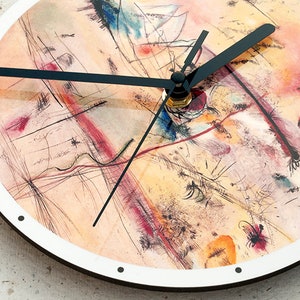 May include: A round clock with a white face and black hands. The clock face features an abstract painting in shades of yellow, orange, red, and blue.