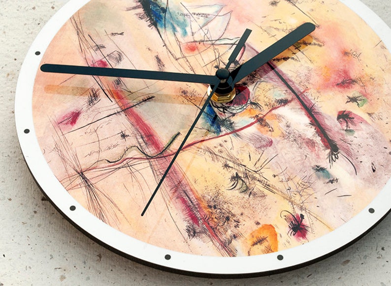 May include: A round clock with a white face and black hands. The clock face features an abstract painting in shades of yellow, orange, red, and blue.