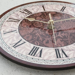 May include: A round clock with a floral design and Roman numeral markings. The clock face is white with a brown floral pattern and the numbers are black. The clock hands are gold.