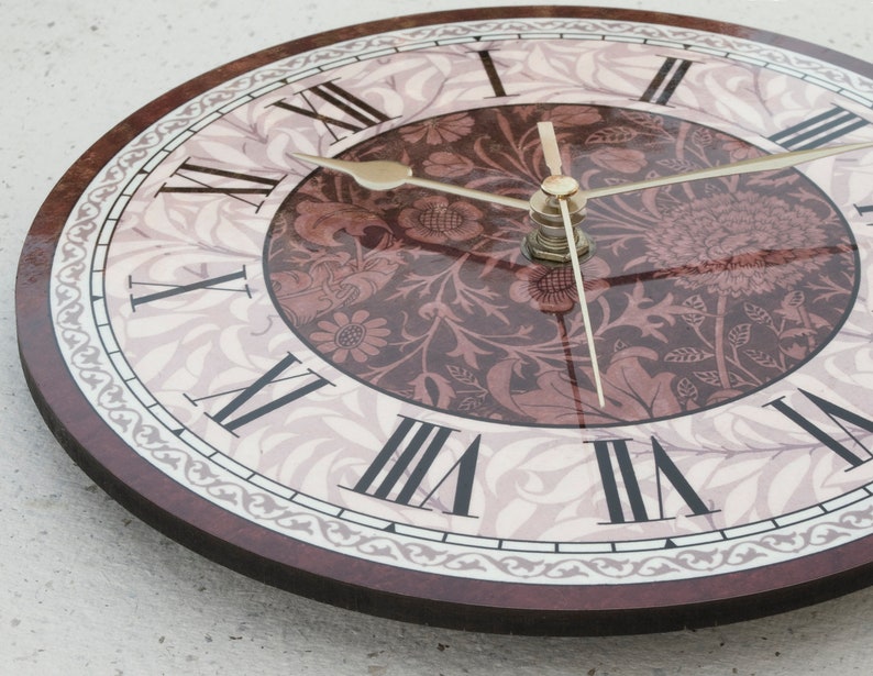 May include: A round clock with a floral design and Roman numeral markings. The clock face is white with a brown floral pattern and the numbers are black. The clock hands are gold.