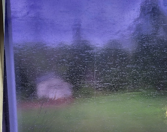 May include: A rectangular, purple-tinted window pane. The glass has a textured surface with visible imperfections. Through the glass, a blurred outdoor scene of green grass and trees is visible, with a hint of a building in the distance.