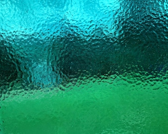 May include: A close-up of a textured glass surface with a blue and green gradient. The glass has a bumpy, uneven texture, creating a blurred effect.