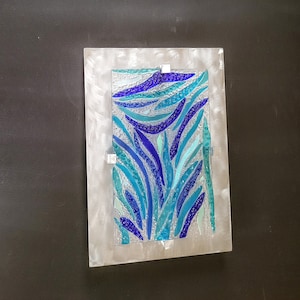 May include: A rectangular wall art piece with a silver frame and a blue and green glass mosaic design. The mosaic features abstract shapes and patterns.