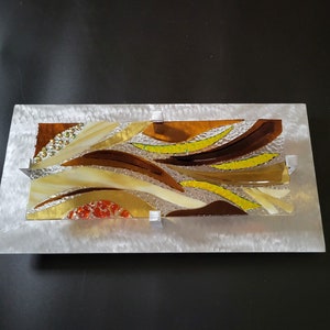 May include: Abstract wall art featuring a mosaic of brown, yellow, and orange glass pieces set in a silver frame.