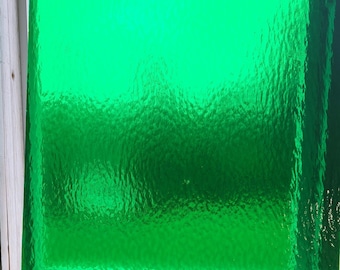 May include: A close-up of a textured, bright green glass panel. The glass has a rippled surface, creating a unique visual effect. The panel is set within a wooden frame, suggesting it could be part of a window or decorative element.
