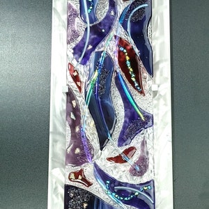 May include: Abstract wall art featuring a silver metal frame with a glass panel. The glass panel is filled with a mosaic of purple, red, and blue glass pieces. The glass pieces are arranged in a random pattern, creating a modern and abstract design.