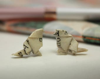 May include: A pair of small origami bird earrings made from recycled book pages. The birds are white with black text.