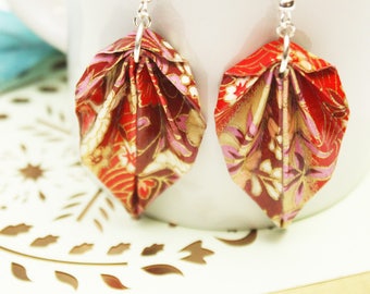 May include: A pair of red and gold origami leaf earrings with a floral pattern. The earrings are made with paper and have silver hooks.