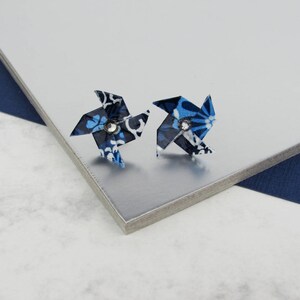 Op de afbeelding: Een paar blauwe en witte stoffen windmolen oorbellen met een strass steentje in het midden.
