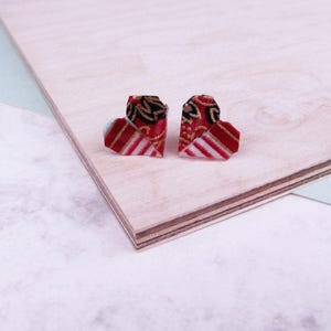 May include: A pair of origami heart earrings made from red, white, and gold patterned paper. The earrings are small and delicate, and they would make a great gift for someone special.