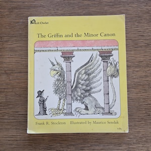 May include: A vintage children's book titled "The Griffin and the Minor Canon" by Frank R. Stockton, illustrated by Maurice Sendak. The cover features a griffin illustration in gray and white, with a small figure in black. The background is yellow.