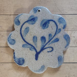 May include: A blue and white ceramic trivet with a floral design. The trivet is shaped like a flower with a hole in the center for hanging.