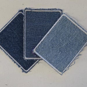 May include: Three rectangular denim fabric patches arranged in a fan shape. The patches feature varying shades of blue, ranging from dark indigo to a light wash, each finished with a white stitched border and frayed edges on the fabric.