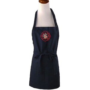 May include: A navy blue apron featuring a red embroidered Maltese cross emblem on the chest. The apron includes a neck strap, a waist tie for securing the garment, and a large front pocket positioned at the bottom section of the fabric.