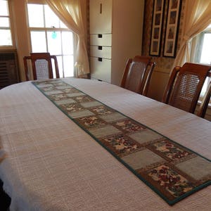 May include: A white tablecloth with a green and brown patchwork table runner. The table runner has a floral pattern and is placed on a dining table with chairs.