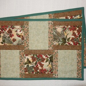 May include: Two green-trimmed quilted table runners with a patchwork design featuring brown, green, and cream fabrics with floral and leaf patterns.
