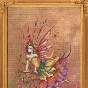 Puede incluir: Obra de arte de punto de cruz de un hada con cabello púrpura, vestida con un vestido de flores y sentada en una rama. El hada tiene alas rosas y rojas y está rodeada de adornos colgantes. La obra está enmarcada en un marco dorado.