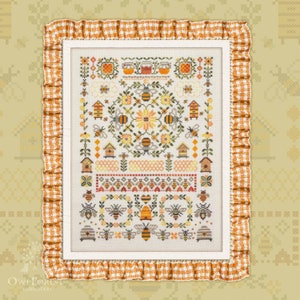 Könnte beinhalten: Kreuzstich-Stickerei mit einem Bienenmotiv. Das Design umfasst Bienen, Bienenstöcke, Honigtöpfe und florale Muster in Gelb-, Orange- und Brauntönen. Das gerahmte Stück hat einen weißen Rand und ist von einem gerüschten, orange-weiß karierten Stoff umgeben.