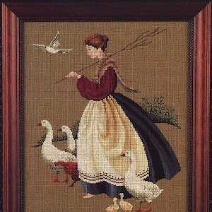May include: A woman in a red and white dress and a blue skirt is herding a flock of white geese. She is holding a stick with a fork on the end. The scene is set against a brown background.