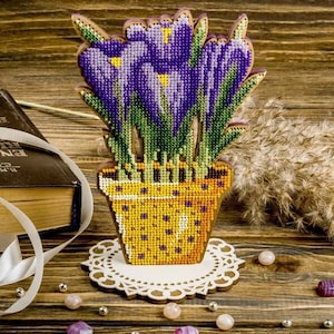 Pode incluir: Um arranjo de flores de crochê roxo e verde em um vaso amarelo com uma base de renda branca.