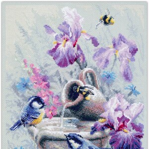 May include: A cross-stitch pattern featuring a stone fountain with a ceramic pitcher pouring water. Two bluebirds perch on the fountain, surrounded by purple irises, pink flowers, and a bee.