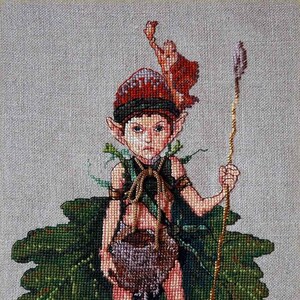 May include: A cross-stitch embroidery of a green-skinned elf wearing a red and green hat, a brown leather pouch, and green leaves. The elf is holding a long, thin, gold-colored stick.