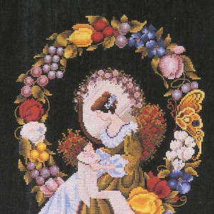 Puede incluir: Un diseño de bordado de punto de cruz que presenta a una mujer sosteniendo un bebé, rodeada de una corona de flores, frutas y una mariposa. La mujer lleva un vestido verde con un cuello de encaje blanco y un delantal blanco. El bebé lleva un vestido azul. La corona está hecha de uvas, manzanas, peras y flores.