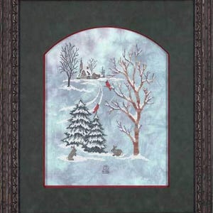 Puede incluir: Una bordadura de punto de cruz enmarcada que representa una escena de invierno con una pequeña casa, árboles y dos conejos en la nieve. El cielo es azul claro con un toque de gris. La bordadura está enmarcada en un marco de madera marrón oscuro con un paspartú verde.