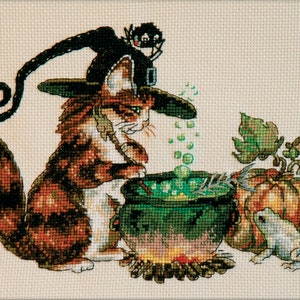 May include: A brown and white cat wearing a black witch hat with a black spider on top, stirring a green cauldron with a wooden spoon. A green frog sits next to a large orange pumpkin.