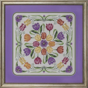 Puede incluir: Un diseño de bordado de punto de cruz blanco con una disposición circular de tulipes coloridas en tonos de morado, naranja, amarillo y rojo. Las tulipes están rodeadas de hojas y enredaderas verdes, creando un patrón floral.