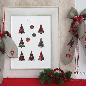 May include: A framed cross-stitch design featuring a white background with nine stylised Christmas trees in red, green, and brown. The trees are decorated with red and white ornaments. The frame is white with a light wood grain finish. A red and white ribbon with a bow is attached to the frame. The image also includes a hessian bag with a red heart and a cross-stitch design of a Christmas tree.