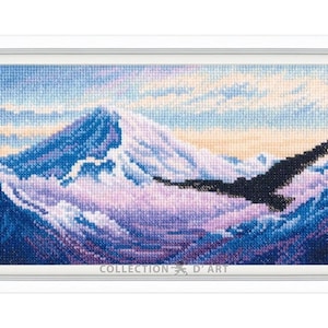 May include: Framed cross-stitch art depicting a mountain landscape with a soaring eagle. The artwork features a color palette of blues, purples, and whites, with a detailed stitch pattern. The frame is white, and the text "COLLECTION D'ART" is visible.