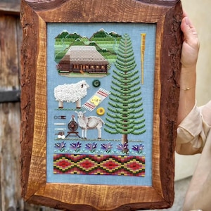 May include: Cross-stitch artwork in a rustic wooden frame. The artwork depicts a rural scene with a house, sheep, and a tall tree. The frame is made of rough-hewn wood, adding a natural, handcrafted feel. The cross-stitch uses various colors to create a detailed image.