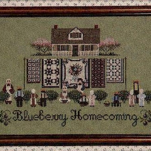Könnte beinhalten: Gerahmtes Kreuzstich-Kunstwerk mit einem Haus, Quilts und Figuren. Das Kunstwerk befindet sich in einem Holzrahmen. Der Text "Blueberry Homecoming" ist unten gestickt. Die Farbpalette umfasst Grün, Braun, Rosa und Weiß.