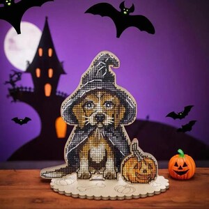 Op de afbeelding: Een houten Halloween-knutselset met een schattig beagle-puppy dat een heksenhoed en een cape draagt. De puppy houdt een kleine pompoen vast en wordt omringd door vleermuizen en een silhouet van een spookhuis.