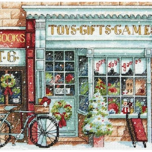 Puede incluir: Un patrón de punto de cruz de una escena de calle nevada con dos tiendas. La tienda de la izquierda es una librería con el letrero "BOOKS" y la tienda de la derecha es una tienda de juguetes con el letrero "TOYS-GIFTS-GAMES". Hay una bicicleta estacionada frente a la librería.