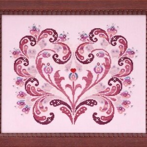 Puede incluir: Un patrón de punto de cruz de un diseño en forma de corazón con intrincados remolinos y detalles florales en tonos de rosa y morado. El corazón está rodeado por un marco.