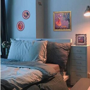 Puede incluir: Un interior de dormitorio con una cama, una c&oacute;moda y tres cuadros enmarcados en la pared. Los cuadros muestran a una ni&ntilde;a con un vestido rojo, un p&aacute;jaro y una luna. La cama tiene un edred&oacute;n azul y blanco y dos almohadas. La c&oacute;moda es blanca con seis cajones. Las paredes son de color azul claro.