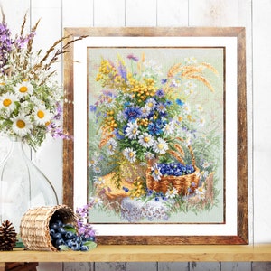Puede incluir: Un bordado en punto de cruz enmarcado que representa un vibrante ramo de flores silvestres, incluyendo margaritas blancas, acianos azules y espigas de trigo doradas, dispuesto en una cesta junto a una pequeña cesta llena de bayas azul oscuro.
