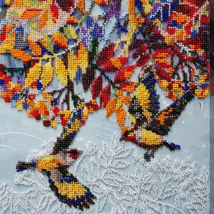Puede incluir: Una obra de arte con cuentas que representa dos pájaros volando a través de un árbol de otoño colorido con hojas rojas, naranjas, amarillas y moradas. El fondo es de color azul claro con hojas de cuentas blancas.