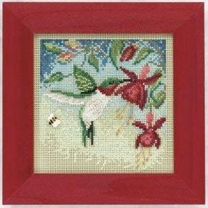 May include: A square cross-stitch embroidery featuring a hummingbird hovering near two red fuchsia flowers and a small bee, set against a light background with green leaves and a blue sky, all enclosed within a solid red wooden frame.