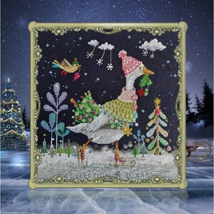 以下が含まれることがあります： ピンクの帽子をかぶって小さなクリスマスツリーを持っているガチョウのクロスステッチパターン。ガチョウは雪景色に立っており、小さな鳥が上空を飛んでいます。パターンは金色のフレームで囲まれています。