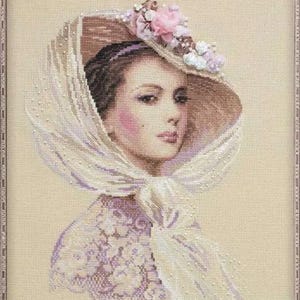 May include: Cross-stitch portrait of a woman wearing a wide-brimmed hat adorned with pink and white flowers. She is also wearing a veil and a lace-trimmed garment. The artwork is framed in a silver-colored frame.