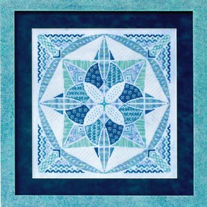 Puede incluir: Obra de arte en punto de cruz enmarcada con un diseño geométrico en tonos azules y blancos. El motivo central es un patrón floral estilizado, rodeado de elementos en forma de estrella y detalles de borde intrincados. El marco es azul claro.