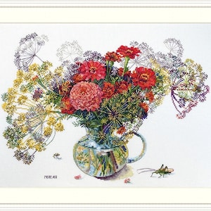 May include: A bouquet of red, orange and yellow flowers in a clear glass vase with a green handle. The vase is sitting on a white surface with a green grasshopper to the right. The flowers are surrounded by green foliage.