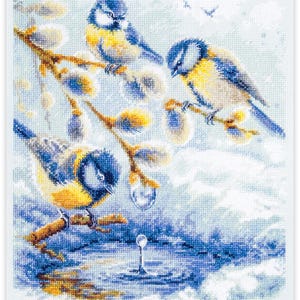 May include: Cross-stitch embroidery of three blue and yellow birds perched on a branch with yellow buds. The birds are set against a backdrop of a blue and white water scene, with a reflective surface and a few birds flying in the distance.