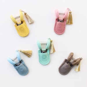 May include: Five colorful, small scissors with matching leather pouches and gold tassels. The scissors are in yellow, pink, blue, teal, and brown. Each pouch has a decorative embossed design.